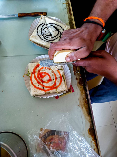 Stock photo of Indian street food vendor shop. Indian street food vendor grating cheese and making testy sandwich for customer. Picture captured under natural light at Kolhapur, Maharashtra, India. - Photo, Image