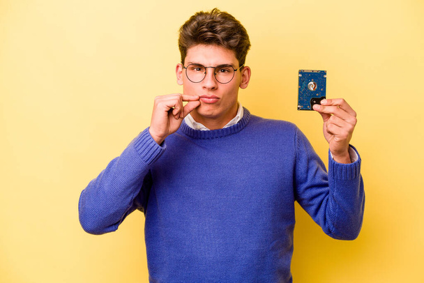 Young caucasian informatics man isolated on yellow background with fingers on lips keeping a secret. - Foto, afbeelding