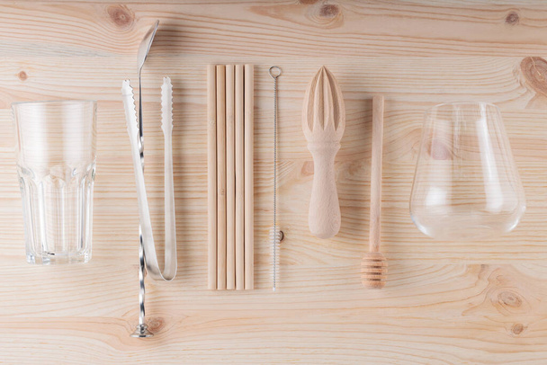 Eco friendly tools for making a cocktail. Bamboo straws, cleaning brush and wooden juicer on the table. Cocktail spoon, ice tongs and glasses for summer drinks. Sustainable lifestyle - Photo, Image