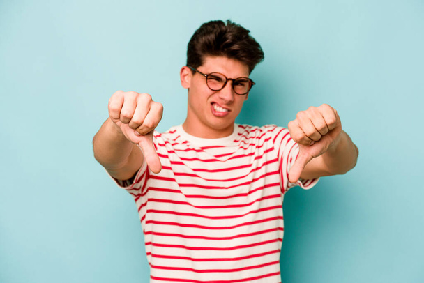Young caucasian man isolated on blue background showing thumb down and expressing dislike. - Foto, Imagen