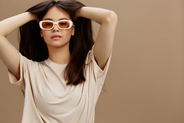 hezká žena v béžovém tričku s brýlemi pózující oblečení módní béžové pozadí. Kvalitní fotografie - Fotografie, Obrázek