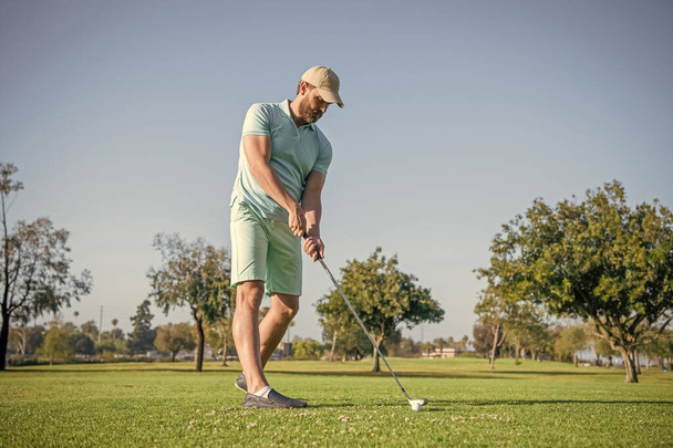 πορτρέτο του παίκτη του γκολφ στο καπέλο με μπαστούνι του γκολφ. τρόπο ζωής των ανθρώπων. ενεργητικός άνθρωπος παίζει παιχνίδι στο πράσινο γρασίδι. καλοκαιρινή δραστηριότητα. επαγγελματική υπαίθρια σπορ. αρσενικό παίκτη γκολφ σε επαγγελματικό γήπεδο γκολφ. - Φωτογραφία, εικόνα