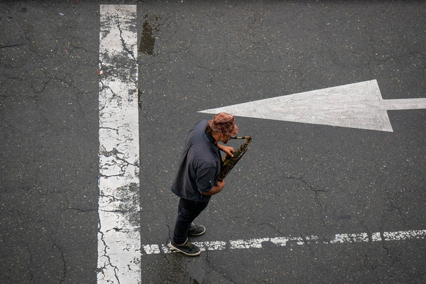 Egy férfi kockás kalapban szaxofonozik az utcán egy tippért. - Fotó, kép