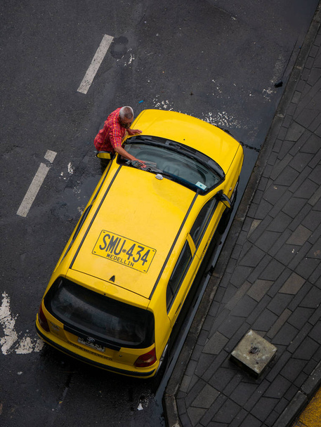 Ο ταξιτζής καθαρίζει το κίτρινο αυτοκίνητό του παρκαρισμένο στην γωνία του δρόμου - Φωτογραφία, εικόνα