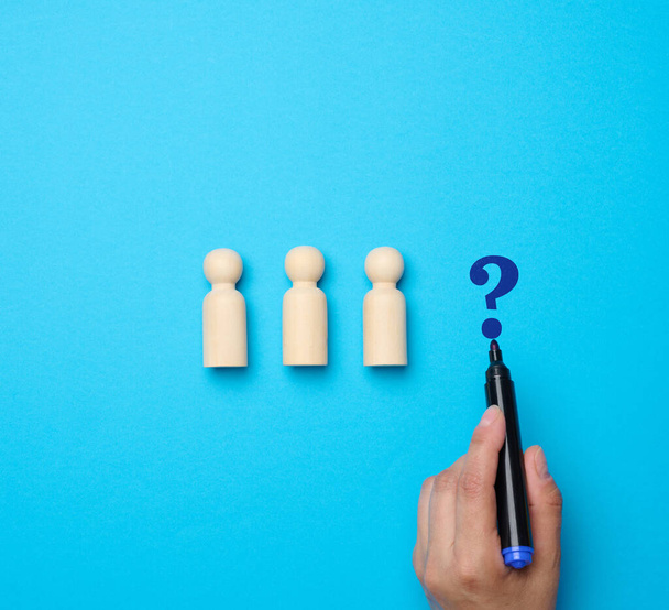 Wooden figures of men and a woman's hand drew a question mark with a marker on a blue background. The concept of searching for a candidate for a vacancy - Photo, Image