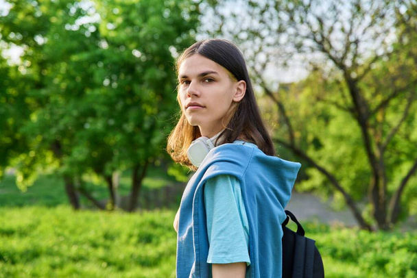 Outdoor portrait of handsome student guy with backpack looking at camera, green park campus background. Young smiling male with long hair hairstyle, copy space. Youth, education, young people concept - Фото, изображение