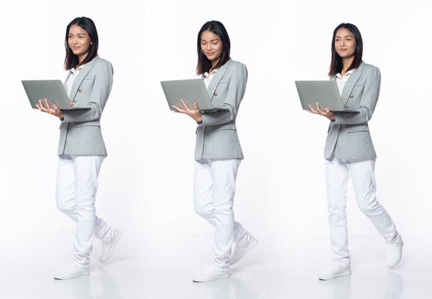 Двадцатилетняя студентка-азиатка, шагающая вправо, в формальных брюках-пиджаках. Улыбка офис женщина нести ноутбук на белом фоне изолированы - Фото, изображение