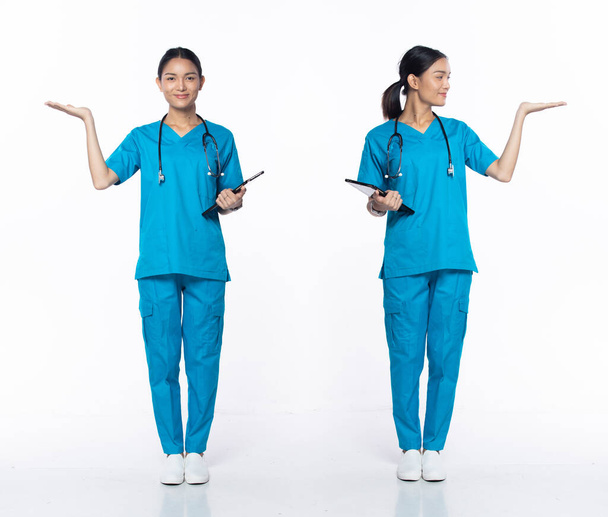 Молода азіатська жіноча клініка 20-х років, що показує порожню долоню, носить сині штани для одягу стетоскоп. Посмішка Самка тримає карту пацієнта над білим фоном. - Фото, зображення