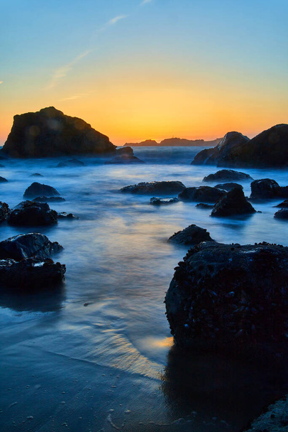 Image of Smooth waves around rocks on beach at golden hour in California - Photo, Image