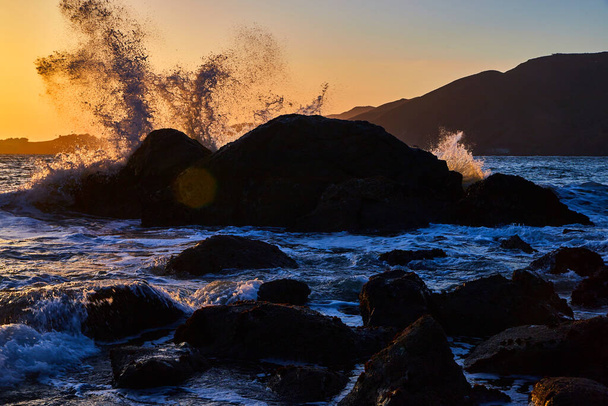 Image of Sun setting by large rocks on ocean with waves crashing - Photo, Image