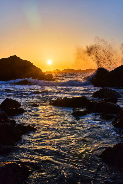 Afbeelding van zonsondergang op het strand van de westkust met golven die over rotsen crashen - Foto, afbeelding