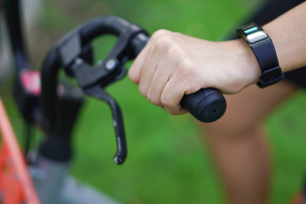 Focus image of the hand holding the bicycle handlebar and the wrist has a smart watch in the park. - Foto, immagini