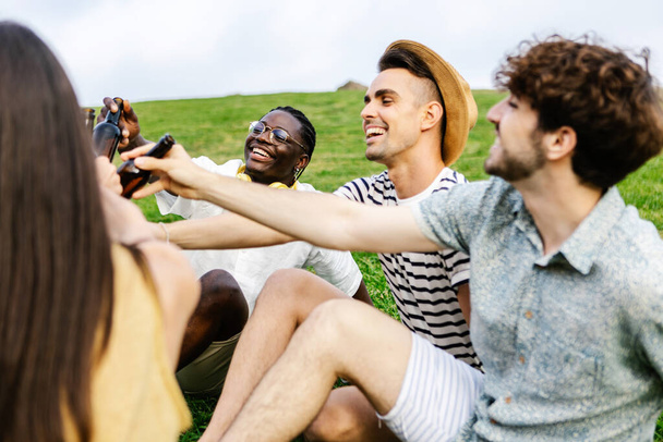 Groep multiraciale vrienden drinken bier genieten van gratis dag in het weekend - Diverse millennial mensen hebben plezier juichen met drankjes ontspannen op het park in de zomer vakantie - Vriendschap en feest - Foto, afbeelding