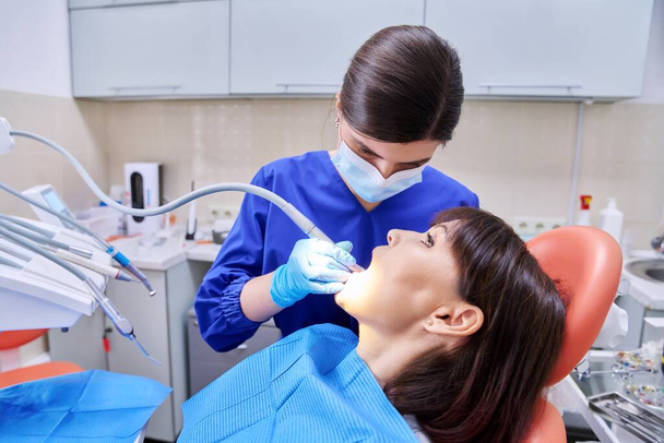 Dental treatment in clinic, woman patient in dental chair, dentist doctor using tools and equipment. Treatment, dentistry, health, teeth care concept - Zdjęcie, obraz