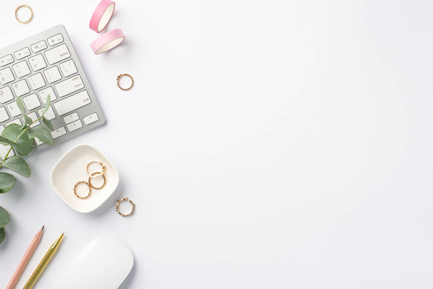 Concepto de negocio. Foto vista superior de la estación de trabajo teclado ordenador ratón eucalipto papelería rosa cinta adhesiva lápiz y anillos de oro sobre fondo blanco aislado con copyspace - Foto, Imagen