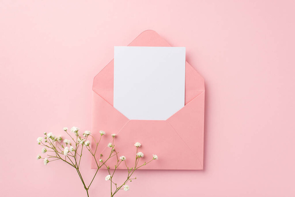 Концепция приглашения. Фото открытого розового конверта с бумажным листом и белыми цветами гипсофилы на изолированном пастельно-розовом фоне с пустым пространством - Фото, изображение