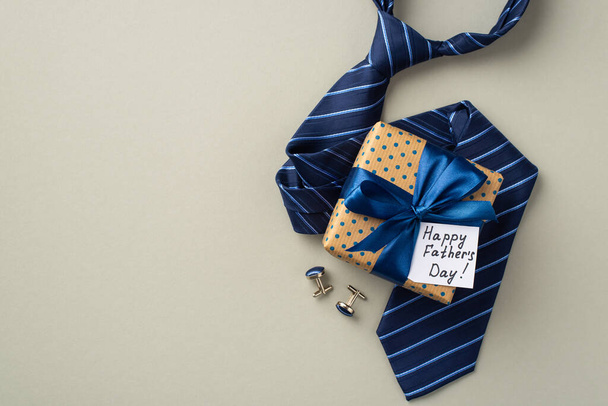 Concepto del Día del Padre. Foto vista superior de la caja de regalo de lunares con lazo de cinta de seda y corbata azul postal y gemelos sobre fondo gris pastel aislado - Foto, Imagen