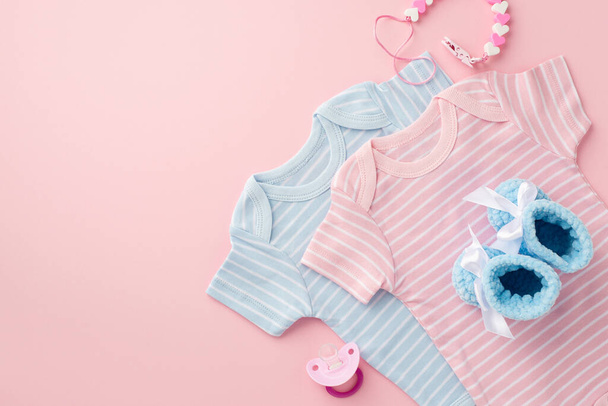 ベビーアクセサリーのコンセプト。ピンクと青の幼児服のボディスーツのトップビューの写真孤立したパステルピンクの背景にニットブーティーとペースメーカーチェーン - 写真・画像