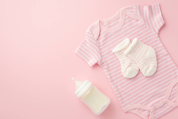 Concept d'accessoires bébé. Photo de vue du dessus de chaussettes de body rose et bouteille sur fond rose pastel isolé avec copyspace - Photo, image