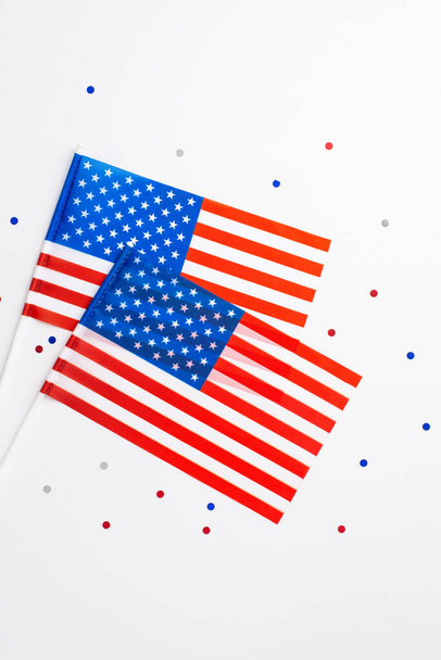 Concetto di Giorno dell'indipendenza degli Stati Uniti. Foto verticale vista dall'alto di due bandiere nazionali e coriandoli su sfondo bianco isolato - Foto, immagini