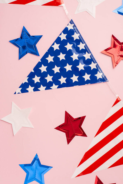Η ιδέα της Ημέρας Ανεξαρτησίας. Πάνω όψη κάθετη φωτογραφία της εθνικής σημαίας γιρλάντα και αστέρια σε απομονωμένο παστέλ ροζ φόντο - Φωτογραφία, εικόνα