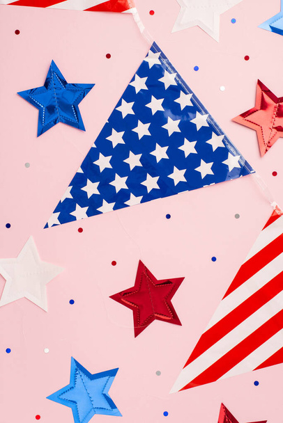 Conceito do Dia da Independência dos EUA. Vista superior foto vertical de estrelas de guirlanda bandeira nacional e confete em fundo rosa pastel isolado - Foto, Imagem