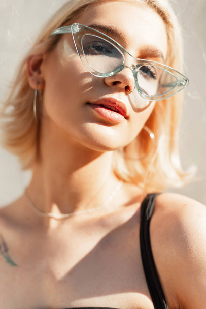 Divatos női nyári portré egy gyönyörű fiatal, friss lányról, kék, stílusos szemüveggel egy napsütéses napon a városban - Fotó, kép