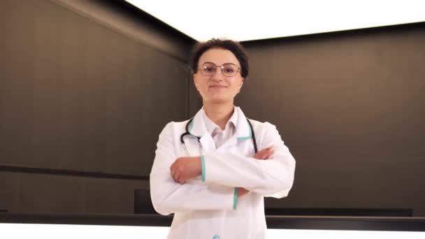 Happy professional woman doctor wearing white medical coat and stethoscope looking at camera. Smiling female physician posing in hospital office. Positive general practitioner close up face portrait - Footage, Video