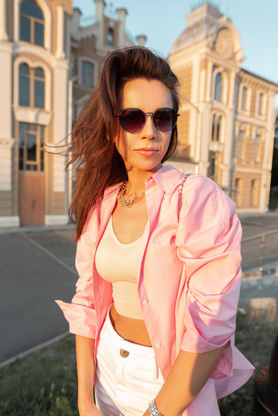 Moda modny hipster kobieta model z fryzurą i okulary przeciwsłoneczne w różowej modnej koszuli i top spacery zbiornika w mieście w letni dzień - Zdjęcie, obraz