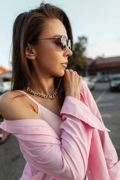 Elegante bella ragazza modello con bijouterie e occhiali da sole in una camicia rosa alla moda e top sexy camminare in città - Foto, immagini