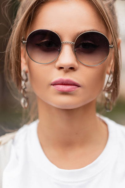 Городской женский портрет модной красавицы-модели с винтажными круглыми солнцезащитными очками в белой футболке на улице. Красота, мода и стиль - Фото, изображение