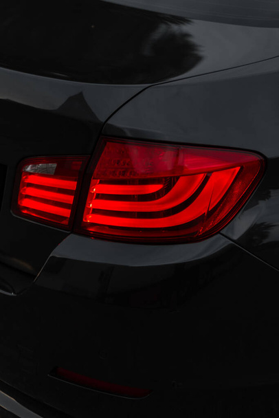 Elegante coche de metal negro con una luz de freno roja sobre un fondo oscuro. Hermoso fondo de pantalla transporte - Foto, imagen
