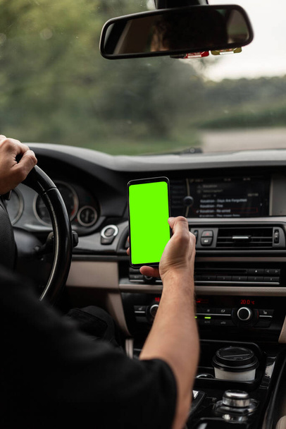 Водій чоловіка керує і тримає смартфон із зеленим макетним дисплеєм
. - Фото, зображення