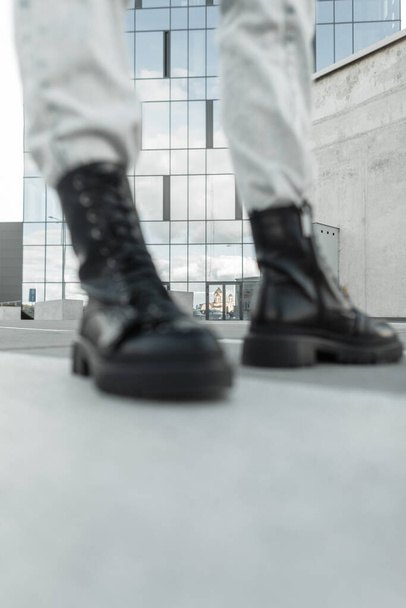 Women's fashionable leather black boots out of focus in the background of the city. Fashionable girl in stylish shoes, concept. Fashion and Style - Photo, Image