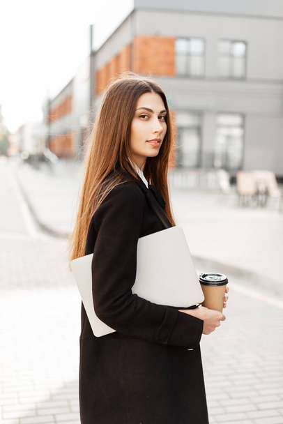 ラップトップとコーヒー付きの黒い服のきれいなファッションビジネス女性は通りを歩くために行く。通りの女性時間管理者 - 写真・画像
