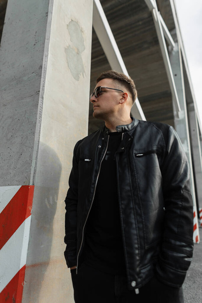 Hipster man in black fashion casual clothes with sunglasses and black leather jacket walks in the city - Fotoğraf, Görsel