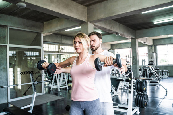 Men teach women practice lifting dumbbell in fitness gym sport activity - Photo, Image