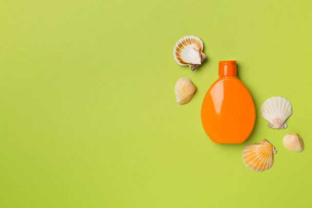 Fles met zonwering crème en zee schelpen op kleur achtergrond, bovenaanzicht. - Foto, afbeelding