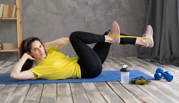 жінка робить фітнес тренування вдома з еластичною смугою опору, вправи для ніг і дупи лежать на підлозі, спорт і фітнес-концепція
 - Фото, зображення