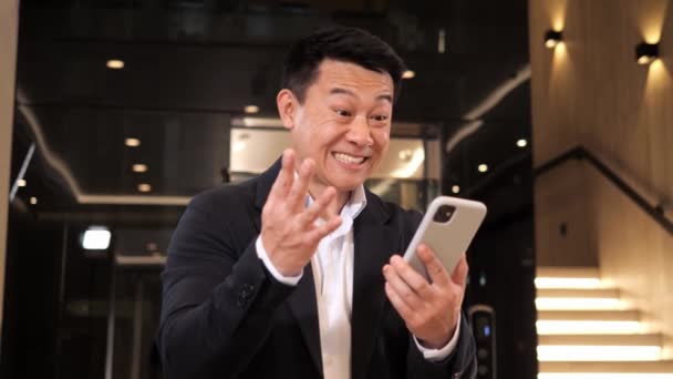 スポーツへの賭け、韓国の驚くべきビジネスマンがSMSメッセージを受信する機会を提供し、幸運な幸せな男はスマートフォンで良いニュースを読む。成功を祝う興奮した男性の勝者携帯電話の勝利 - 映像、動画