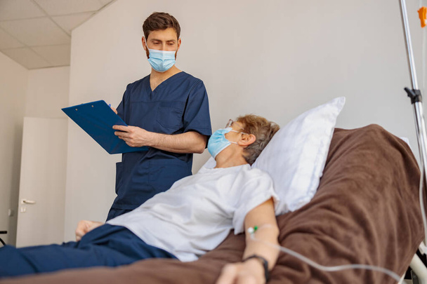 Covid-19 salgını sırasında hastane koğuşunda hasta semptomları yazan bir doktor. Yüksek kalite fotoğraf - Fotoğraf, Görsel