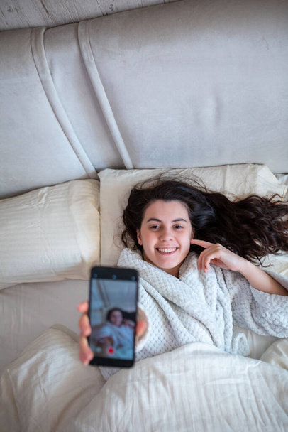 young happy woman taking selfie story laying down in bed morning time - Φωτογραφία, εικόνα