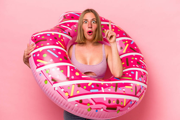 Young caucasian woman holding an air mattress isolated on pink background having some great idea, concept of creativity. - Фото, зображення