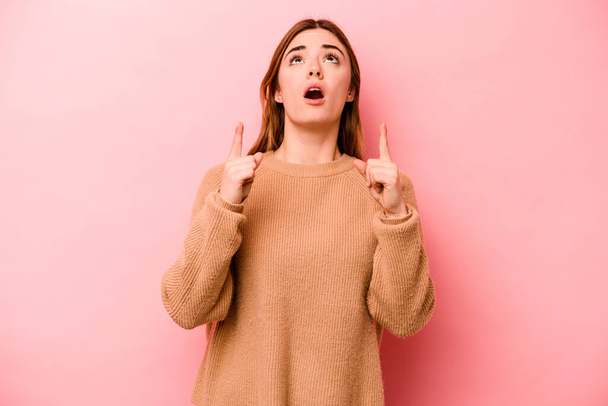 Young caucasian woman isolated on pink background pointing upside with opened mouth. - Fotó, kép