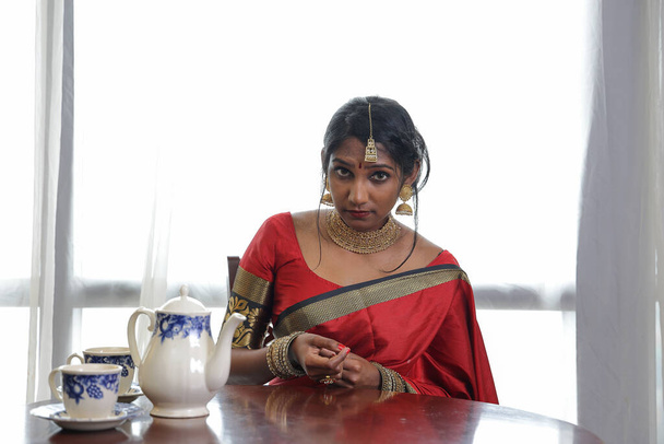 Indiase vrouw dragen rode oranje saree sieraden choker set ketting jhumka oorbel maang tikka taille ketting stand pose look zie glimlach stemming expressie look  - Foto, afbeelding