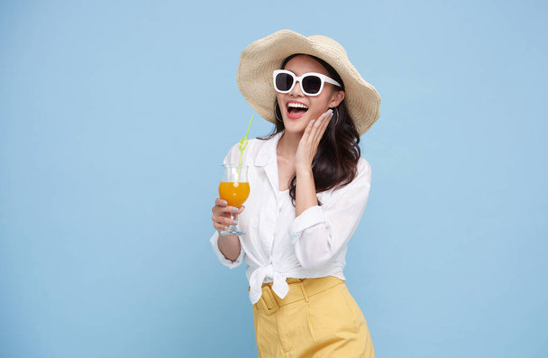 美しい笑顔アジアの女性で夏の衣装にオレンジジュースのガラスがカラフルな青の背景に隔離されています. - 写真・画像