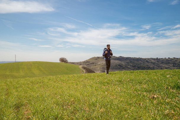 Szakállas fiatalember, aki egyedül sétál a zöld réten, hátizsákkal a hátán - a sport és az önfejlesztés fogalma - Fotó, kép