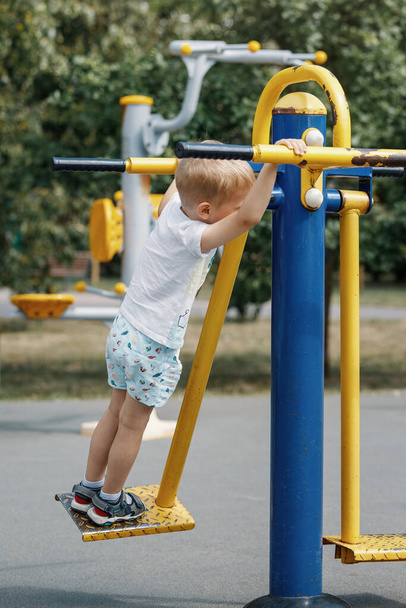 Маленький хлопчик гойдається і виконує вправи на відкритому тренажерному майданчику
. - Фото, зображення