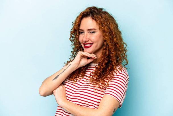 Young ginger caucasian woman isolated on blue background smiling happy and confident, touching chin with hand. - Фото, зображення