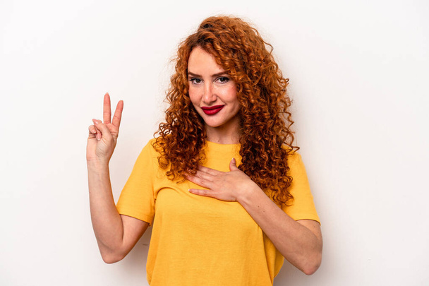 Νεαρή κοκκινομάλλα καυκάσιος γυναίκα απομονωμένη σε λευκό φόντο παίρνει όρκο, βάζοντας το χέρι στο στήθος. - Φωτογραφία, εικόνα